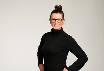 Auf dem Bild ist Dr. Claudia Viehweger, die Chief Sustainability Officer von Scout24 zu sehen. Sie hat die Haare in einen Dutt gebunden, trägt eine Brille und ein schwarzes Kleid. Sie lächelt in die Kamera. 