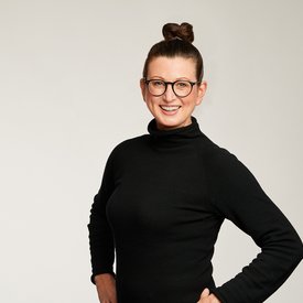 Auf dem Bild ist Dr. Claudia Viehweger, die Chief Sustainability Officer von Scout24 zu sehen. Sie hat die Haare in einen Dutt gebunden, trägt eine Brille und ein schwarzes Kleid. Sie lächelt in die Kamera. 